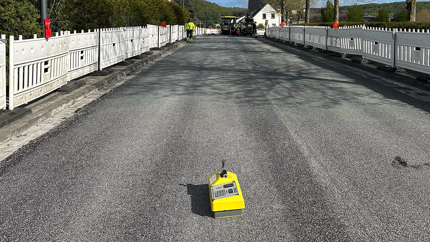 bpf Leistungsseite Asphalt und Strasse Header: Neu asphaltierte, abgesperrte Straße mit gelbem Messgerät zur Qualitätskontrolle im Vordergrund und Straßenbaumaschinen im Hintergrund.
